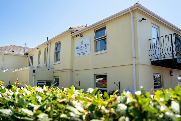 Mount Olivet Nursing Home's front elevation, with the reception sign and a flowering hedge in the foreground
