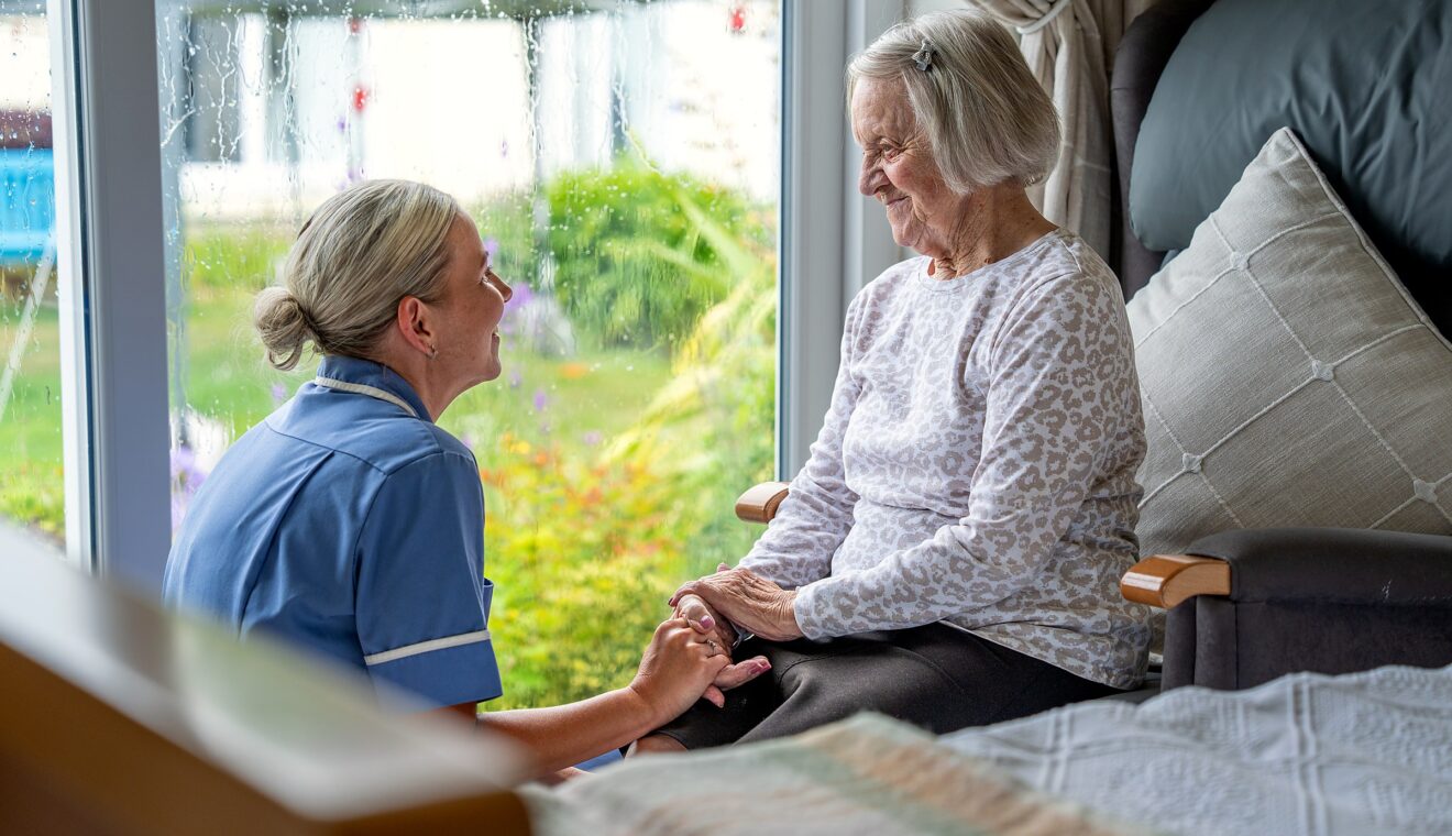A staff member holding a resident's hand by the window