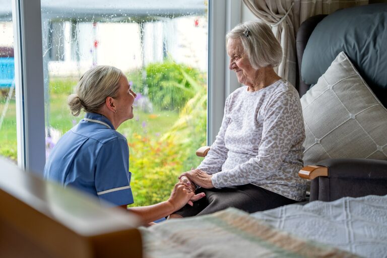 A staff member holding a resident's hand by the window